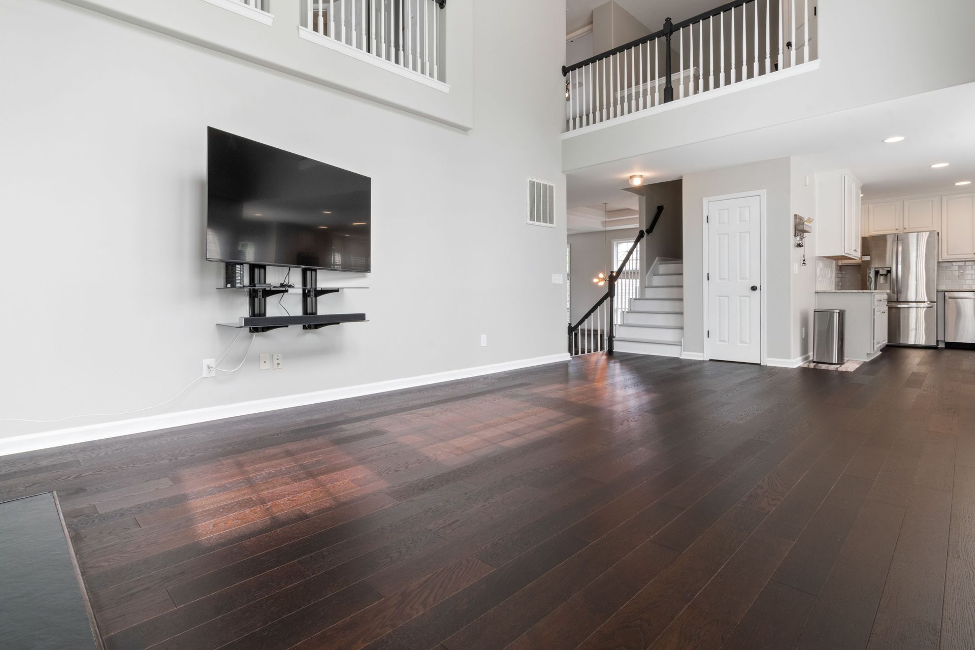 Spacious modern living room with dark wood flooring and a mounted TV, highlighting minimalist design.